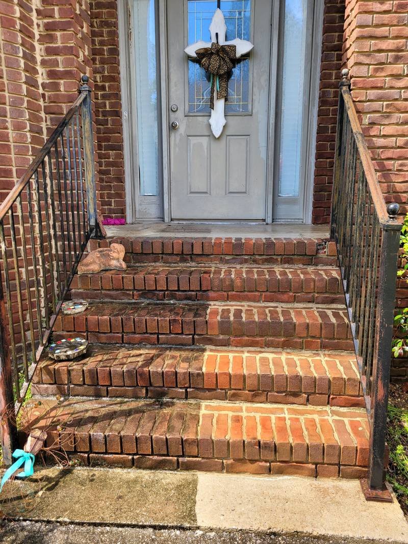 Brick front steps part-way through a pressure wash, with a clear line between the cleaned and dirty brick